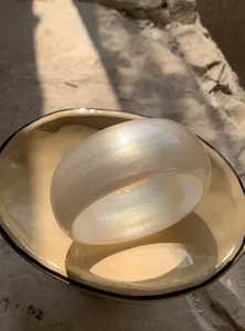 Close-up of a wide iridescent white resin bangle with a pearlescent shimmer finish.