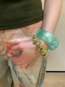 Close-up of Y2K style chunky iridescent green resin bangle and gold bead bracelet
