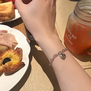 Detail view of a minimalist silver heart charm bracelet on a model's wrist
