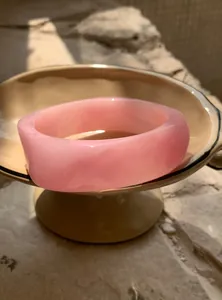 Detailed view of a thick pink resin bangle with marble texture on a beige stand.