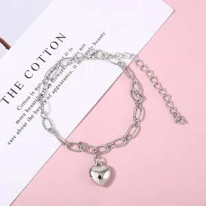 Close-up detail of silver heart pendant chain bracelet on a minimalist pink background