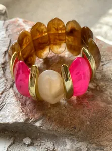 Close-up detail of vibrant pink and amber resin bracelet with metallic gold accents
