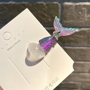 Nahaufnahme einer Meerjungfrau-Haarspange mit Glitzerherz auf weißer Karte, Ziegelwand.