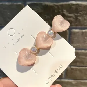 Detailaufnahme einer rosa Haarspange in Herzform mit Glitzer und Perlen auf einer Karte
