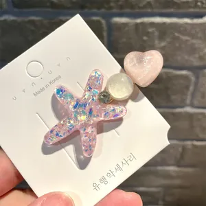 Detailansicht einer rosa glitzernden Seestern- und Herz-Haarklammer auf einer Karte.