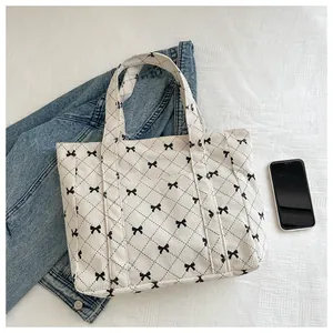 Detail view of a corduroy tote bag featuring a black bow pattern on a cream background