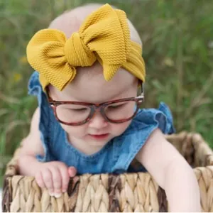 Close-up detail of a mustard yellow textured bow headband worn by a baby model outdoors