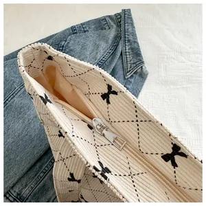 Close-up view of a cream corduroy tote bag showing the metal zipper and black bow patterns