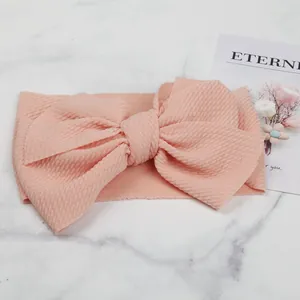 Close-up detail of soft peach baby headband featuring waffle texture and large bow design
