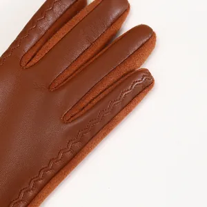 Close-up view of brown faux leather and suede gloves featuring intricate wavy stitching details