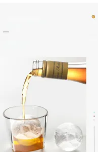 Große kristallklare Eiskugel für Whiskey beim Eingießen in ein Glas aus einer Flasche
