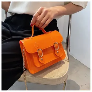 Detail view of a bright orange mini jelly satchel bag with gold chain and buckles
