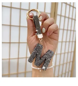 Close-up of a rhinestone-studded letter M keychain with a gold ring and black strap