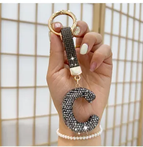 Close-up of a sparkling rhinestone letter C keychain held by a hand with pearl bracelet.
