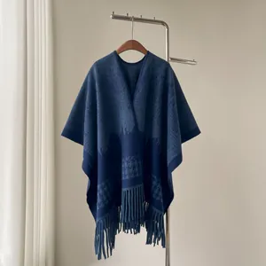 Detailed view of a thick blue houndstooth shawl poncho with tassels hanging on a rack