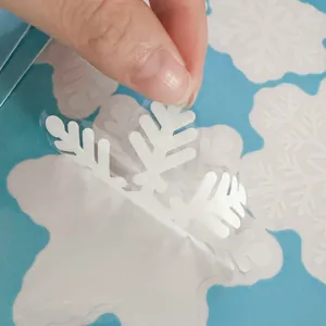 Gros plan montrant l'application d'un sticker flocon de neige pour fenêtre de Noël