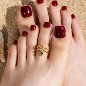 Close-up detail of a gold hollow geometric toe ring with a green gemstone on beach sand