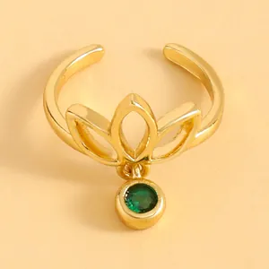 Macro view of a gold lotus hollow toe ring featuring a dangling round green gemstone charm.