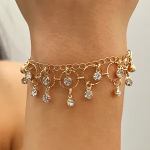 Close-up detail of golden chain bracelet with dangling zircon stones and circular charms.