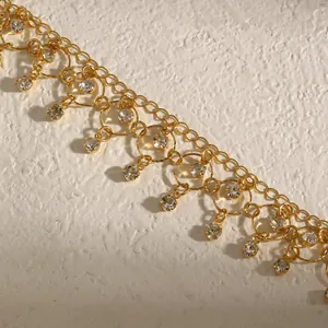 Macro detail of gold-plated choker with sparkling zircon tassels on textured background.