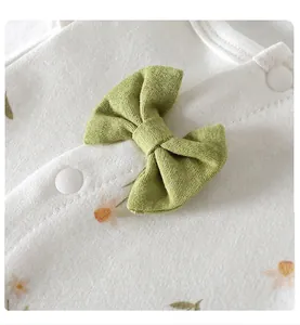 Detailed view of a green bow and snap buttons on soft white floral baby romper fabric
