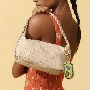 Close-up detail of ocean series tinned fish bag charm on a beige woven shoulder bag