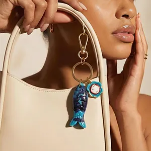 Close-up of blue marbled fish bag charm on a cream handbag with a gold metal clasp