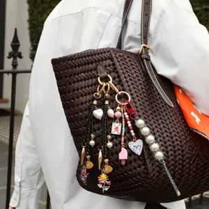 Détail de breloques en acier inoxydable coloré et perles sur un sac tressé marron