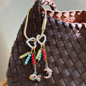 Gros plan d'un bijou de sac coloré fait main avec perles et pendentifs cœur et poisson.