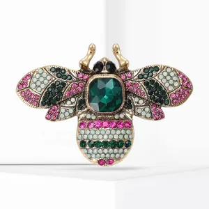 Detailed macro view of a vintage gold bee brooch featuring colorful emerald green rhinestones