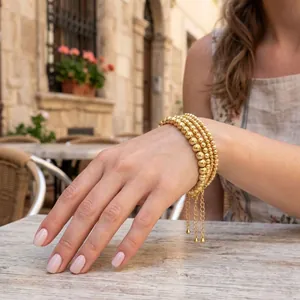 Detailed view of stacked gold-plated bead bracelets with dangling chains worn on a wrist