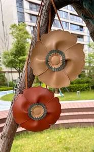 Detail view of cute flower-shaped kids' crossbody bags hanging on a tree branch outdoors