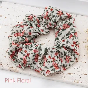Close-up view of a pink floral print cloth scrunchie on a white textured stone base.