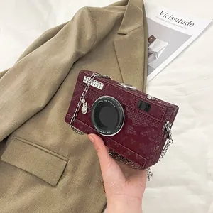 Detailed macro view of a burgundy snakeskin textured camera-shaped crossbody box bag