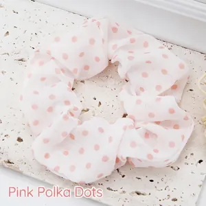 Close-up of a stylish white fabric scrunchie with cute pink polka dot patterns.