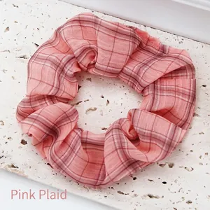 Detailed view of a pink plaid fabric scrunchie on a textured white stone surface.