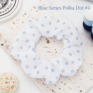 Macro view of a white fabric scrunchie with blue polka dots on a textured slab.