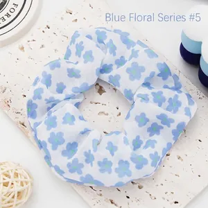 Close-up of a blue floral fabric scrunchie with delicate flower patterns on white base.
