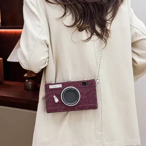 Stylish vintage camera shaped hard box crossbody bag in burgundy worn over a cream coat