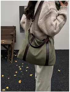 Grande borsa tote in tela verde con cinturini marroni a contrasto in ambientazione esterna.