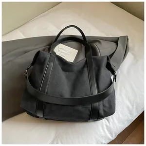Grande borsa tote in tela nera con tracolla esposta su biancheria neutra.