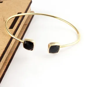 Close-up of gold stainless steel open cuff bracelet with square black gemstones