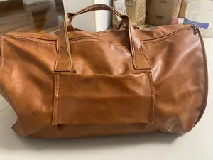 Detailed view of brown faux leather travel garment bag with carry handles and outer pocket.