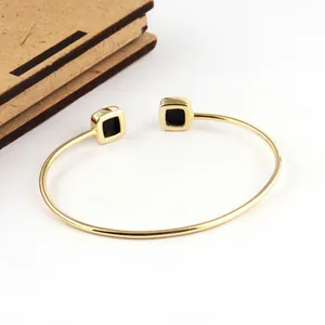 Close-up of a gold stainless steel open cuff bracelet with sleek square black ends.