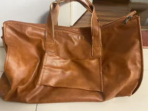 Detailed view of a brown faux leather travel garment bag featuring a large front pocket