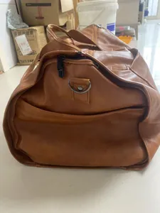 Close-up of a tan faux leather travel duffel bag with side pocket and strap attachment