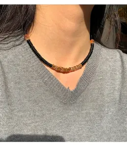 Detail view of a black coconut shell and gold copper alloy necklace worn on a model.