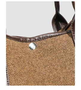 Détail de sac cabas en tweed à chevrons avec bordure en cuir et bouton.