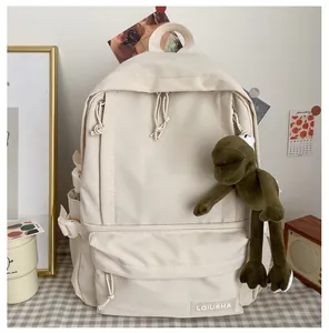 Detail view of a beige forest-style backpack featuring a green frog plush keychain.