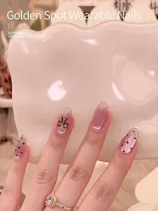 Close-up of nude pearlescent press-on nails with black dots and rhinestone bow detail.
